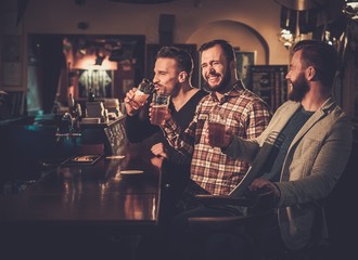 Cheerful old friends having fun and drinking draft beer at bar counter in pub.