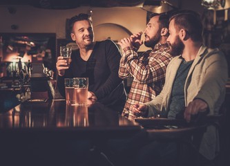 Cheerful old friends having fun and drinking draft beer at bar counter in pub.