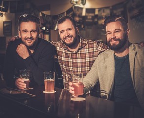 Cheerful old friends having fun and drinking draft beer at bar counter in pub.