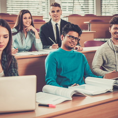 Multinational group of cheerful students taking an active part in a lesson while sitting in a lecture hall.