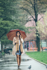 Young woman with umbrella at the park, talking on the phone