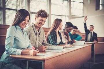 Multinational group of cheerful students taking an active part in a lesson while sitting in a lecture hall.