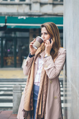 Young woman at the street drinking coffee and talking on the phone
