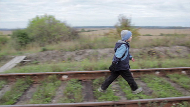 boy going by rail/child goes on railway track in autumn in cloudy weather
