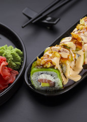 Sushi with avocado and salmon with delicious sauces on a black plate. Crunch roll.