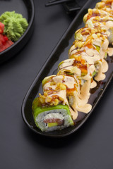 Sushi with avocado and salmon with delicious sauces on a black plate. Crunch roll.
