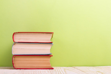 Stack of hardback books, diary on wooden deck table and green background. Back to school. Copy Space. Education background
