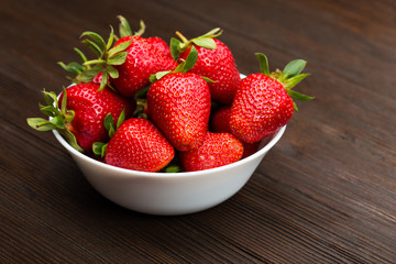 Fresh ripe strawberries in a simple white bowl, on dark wooden table