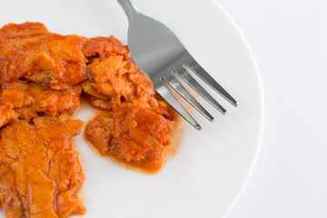 Spicy flavored pink salmon on a plate with a fork atop an off white table cloth.