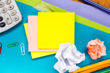 Office table desk with set of colorful supplies, white blank note pad, cup, pen, pc, crumpled paper, flower on blue background. Top view and copy space for text