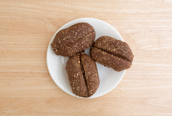 Multi-grain rolls on a white plate atop a wood table top.