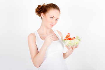 Beautiful young pregnant woman / teenager in white cloth eating healthy fresh salad with vegetables