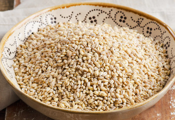Barley in ceramic bowl on  wooden board.