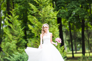 Obraz na płótnie Canvas Beautiful bride with wedding bouquet of flowers outdoors in green park.