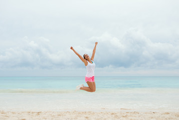 Fitness happy woman jumping for celebrating workout success and summer vacation freedom at the beach.