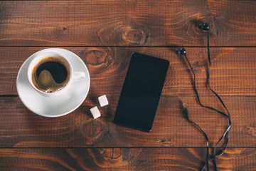 beautiful new black mobile phone with headphones, a Cup of coffee with two lumps of sugar cubes on old wooden background