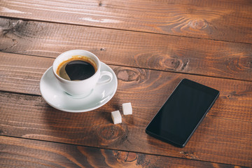 beautiful new black mobile phone, a Cup of coffee with two lumps of sugar cubes on old wooden background
