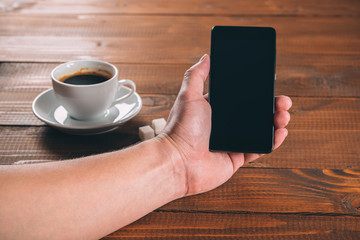 man hand holding a phone with isolated screen  on the wooden background with cup of coffee