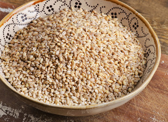 Barley in a ceramic bowl on a wooden board.