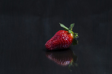 Big red fresh strawberry placed on a mirror black wooden table