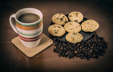 Cookies, coffee beans and mug of coffee on the brown table. Vintage style photo. 