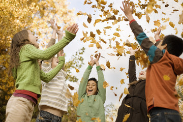 A group of children, young people, throwing fallen autumn leaves into the air, 