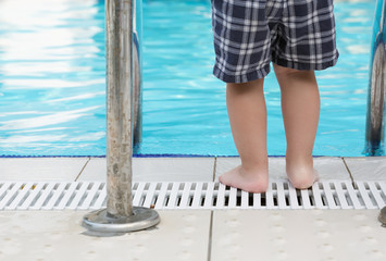 Child's feet standing close to a handrail by a swimming pool