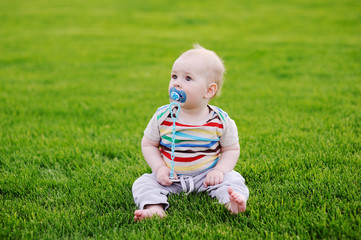 barefooted baby with a pacifier is sitting in the grass