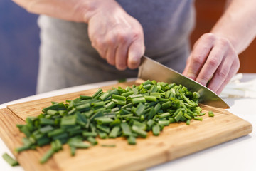 man chopped green onion on the board. Wooden table