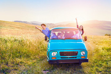 Young frieds leaning out of campervan, green sunny nature