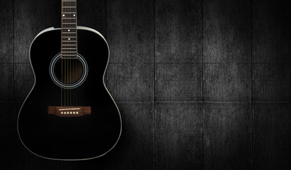 Black acoustic guitar on dark black wooden background.