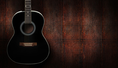 Black acoustic guitar on dark red wooden background.