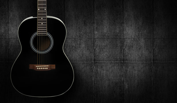 Black acoustic guitar on dark black wooden background.