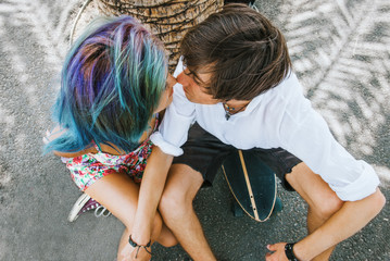 Young couple is kissing under the palm tree,sitting on the skateboard - 105445714
