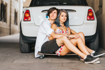 Couple hugging each other sitting on the skateboard desk in front of the car  - 105445720