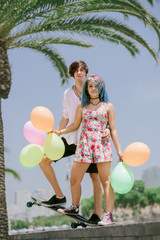 Young couple standing on the skateboard with colorful balloons  - 105445731