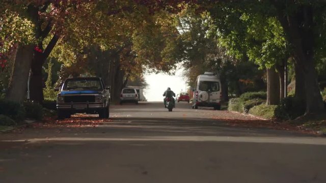 Man Riding Motorcycle Away from Camera in City Streets during Fall Season