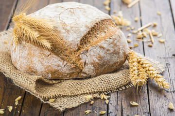 Hogaza de pan de cereales variados sobre arpillera rústica con espigas de trigo y centeno para la...
