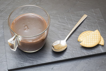 cup of cocoa on a slate tray with a spoon and a cookie
