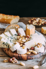 Cheese plate: Emmental, Camembert cheese, blue cheese, bread sticks, walnuts, hazelnuts, honey on wooden table