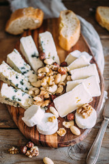 Obraz na płótnie Canvas Cheese plate: Emmental, Camembert cheese, blue cheese, bread sticks, walnuts, hazelnuts, honey on wooden table