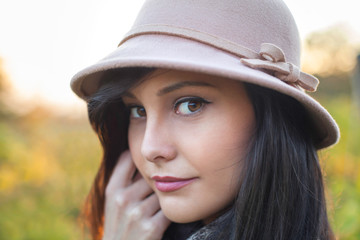 Beautiful woman posing with a hat, looking at the camera. Autumn and spring portrait of beauty female model. Close up of caucasian young girl. Elegance lady in nature
