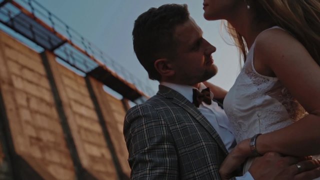 Groom holds his bride's waist on a background of a dam