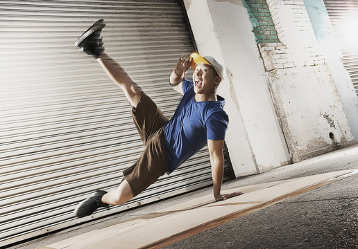 A young man breakdancing on the street of a city, balancing on one hand with his legs apart, 