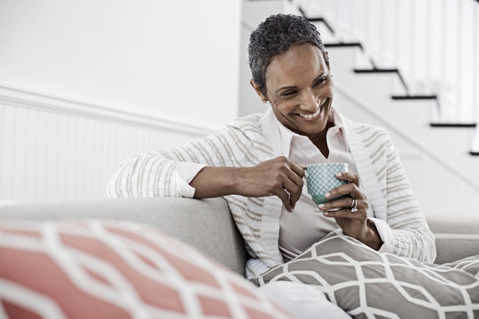 A woman seated on a sofa, holding a cup of coffee, 