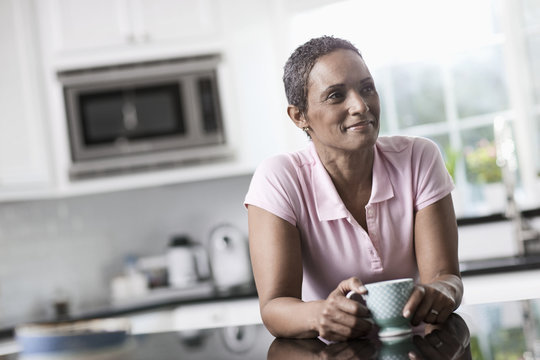 A woman leaning on the smooth countertop of her kitchen unit, with a cup of coffee,