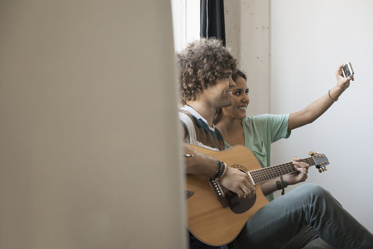 Young Man Playing Guitar And Woman Beside Him Taking  Selfie With  Smart Phone