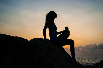 the beautiful girl sitting on stones and looking in a distance, the girl at sunset to meditate in silence, beautiful telo.concept .Siluet lonely girl sitting on the precipice of a cliff at sunset. 