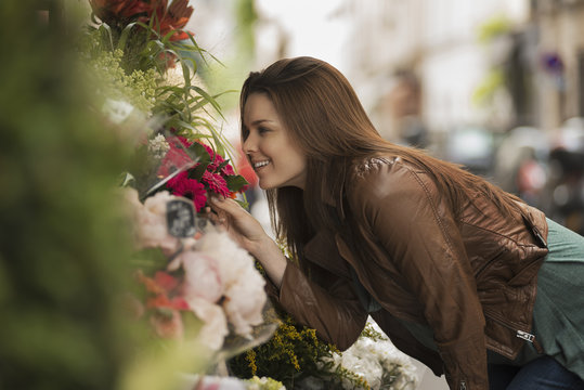 A woman bending to smell the scent of flowers at a stall on the street, 