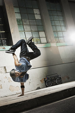 A young man breakdancing on the street of a city, doing a one handed handstand,